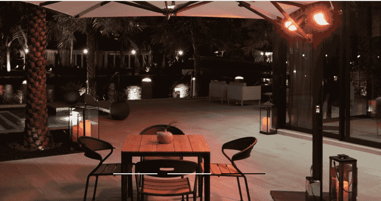Cantilever umbrella with integrated radiant heaters over patio dining at night